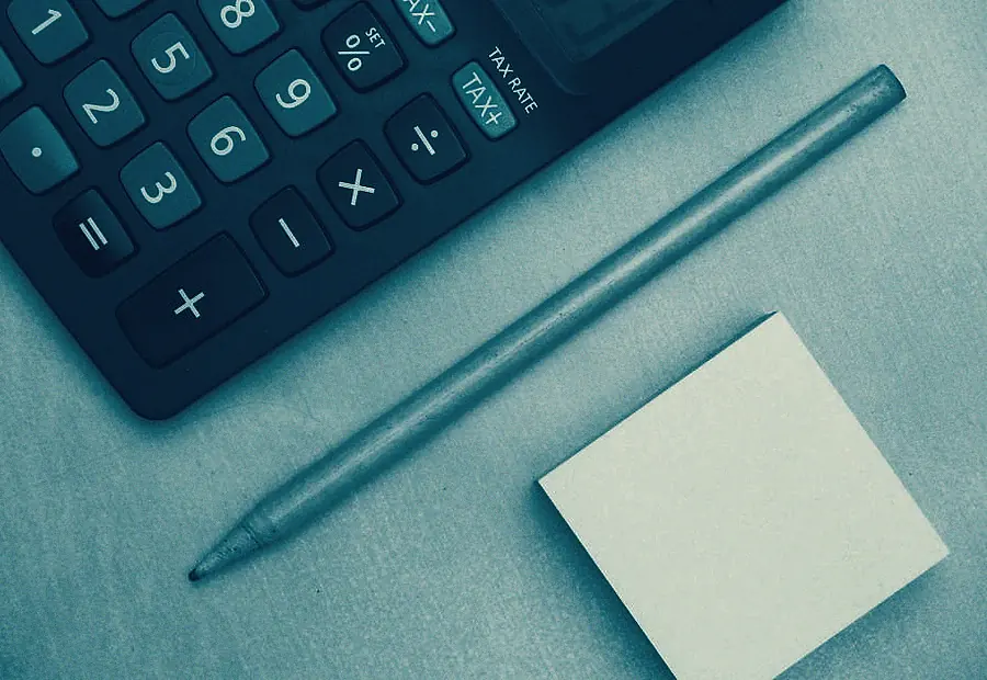 Calculadora, bolígrafo y una nota adhesiva sobre una mesa de trabajo