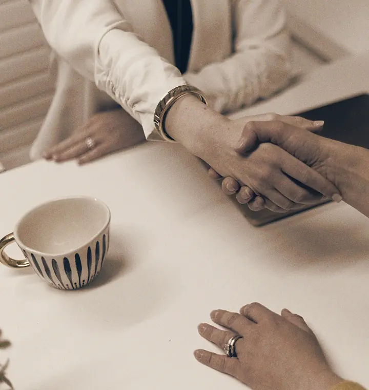 Dos personas se dan la mano sobre una mesa con dos tazas de café