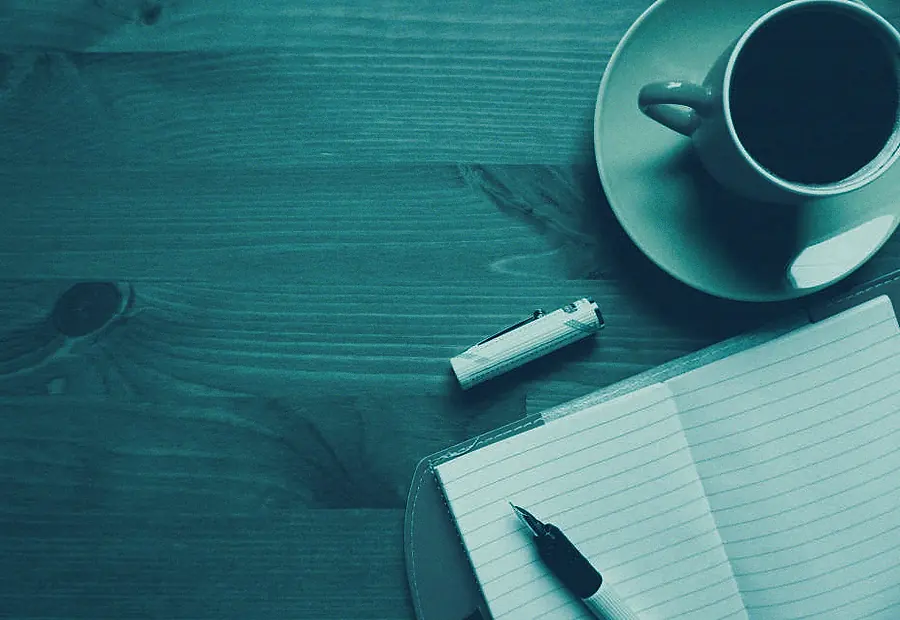 Cuaderno abierto, bolígrafo y una taza de café sobre una mesa de madera